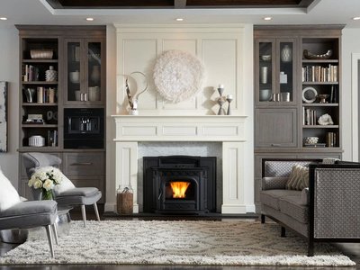 Black pellet stove burning inside a white fireplace surround in an elegant living room with built-in shelving and gray seating.