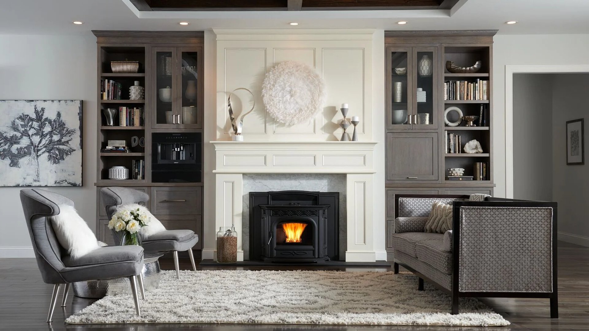 Black pellet stove burning inside a white fireplace surround in an elegant living room with built-in shelving and gray seating.