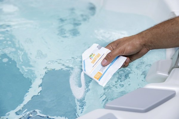 A man's hand sprinkling shock into a hot tub.