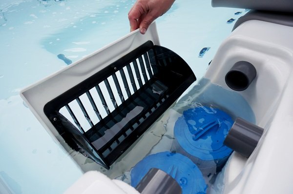 The person is lifting out the filter basket or skimmer basket, which catches larger debris like leaves, hair, and dirt before the water passes through the filter cartridges below.