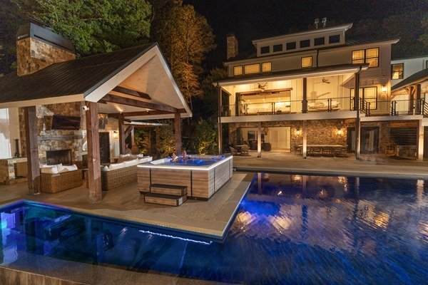 A couple sitting in their hot tub in the backyard next to an inground pool and outdoor furniture.