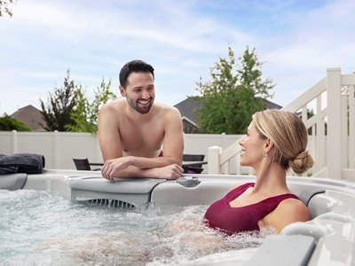 A man sitting outside of a hot tub and a woman sitting in the hot tub and they are having a conversation.