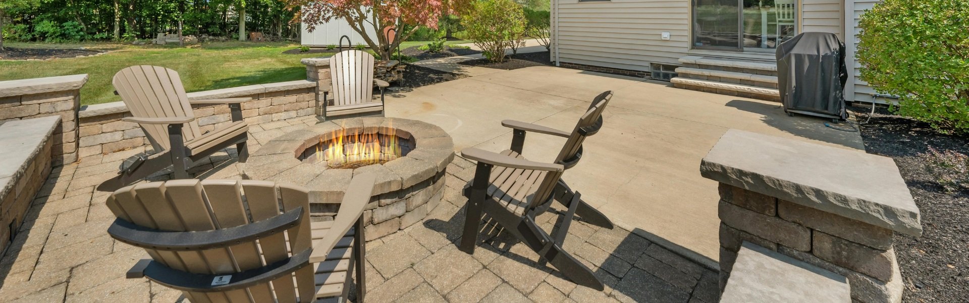 A backyard with a fire pit in the middle and chairs around it.