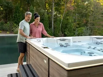 Couple standing beside a modern outdoor hot tub overlooking a peaceful New Hampshire lakeside setting, illustrating the comfort and year-round value of hot tub ownership in the Granite State.