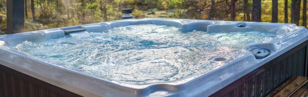 Outdoor hot tub with bubbling water surrounded by a sunlit wooded landscape in spring
