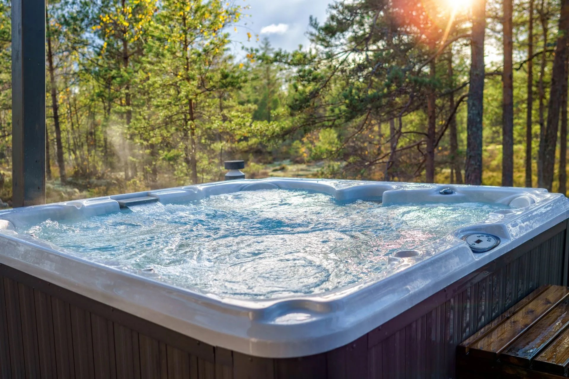 Outdoor hot tub with bubbling water surrounded by a sunlit wooded landscape in spring